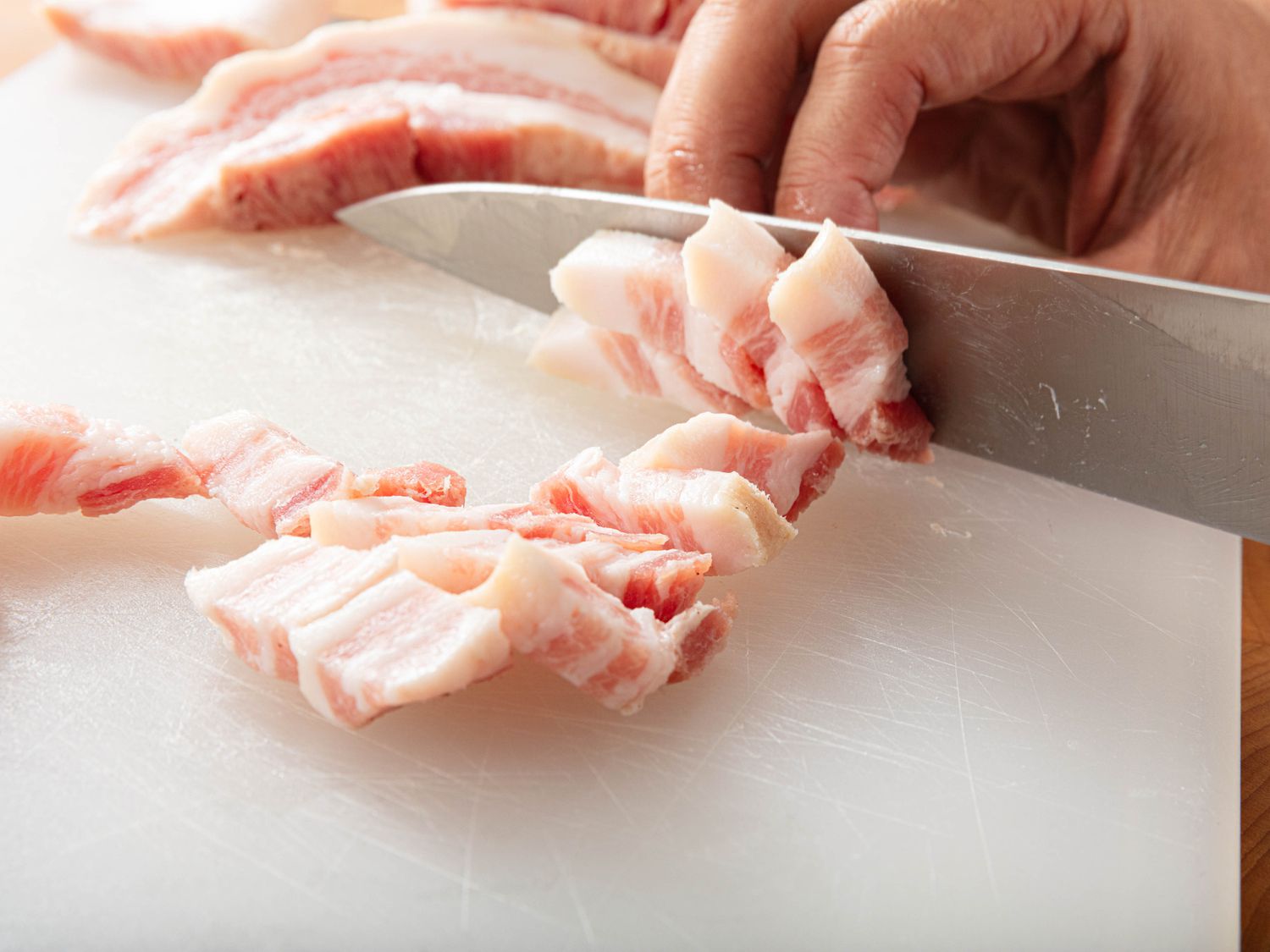 Lardon slab being sliced with large knife on cutting board 