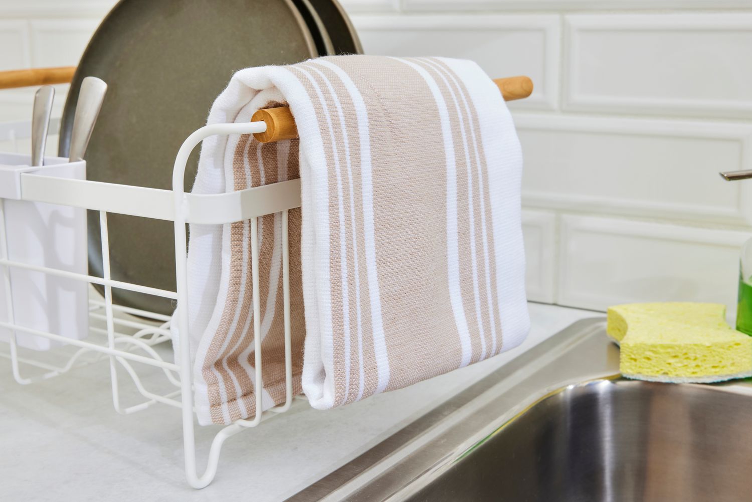 A brown and white striped kitchen towel folded and hanging from the end of a dish rack.
