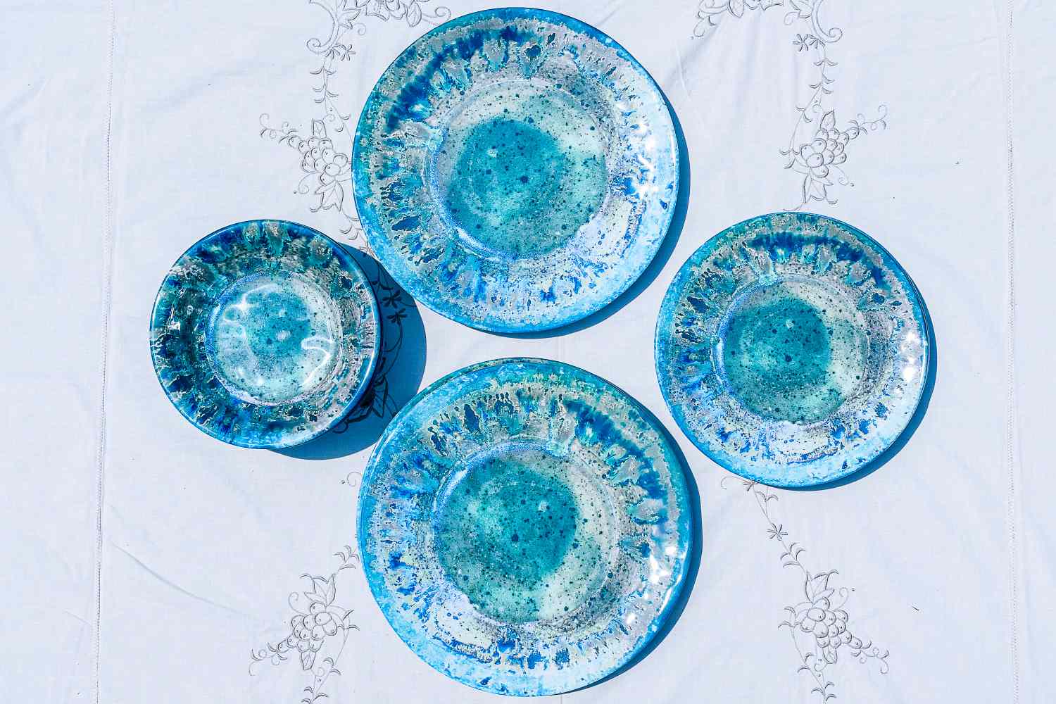 Set of four Certified International Radiance Teal Melamine Dinnerware Set ceramic plates and a bowl arranged on a linen cloth