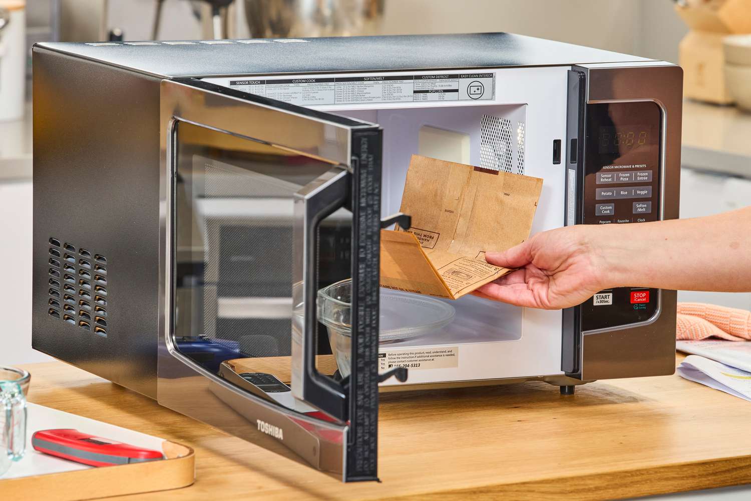 A hand placing a popcorn bag into the Toshiba EM131A5C-BS Microwave Oven