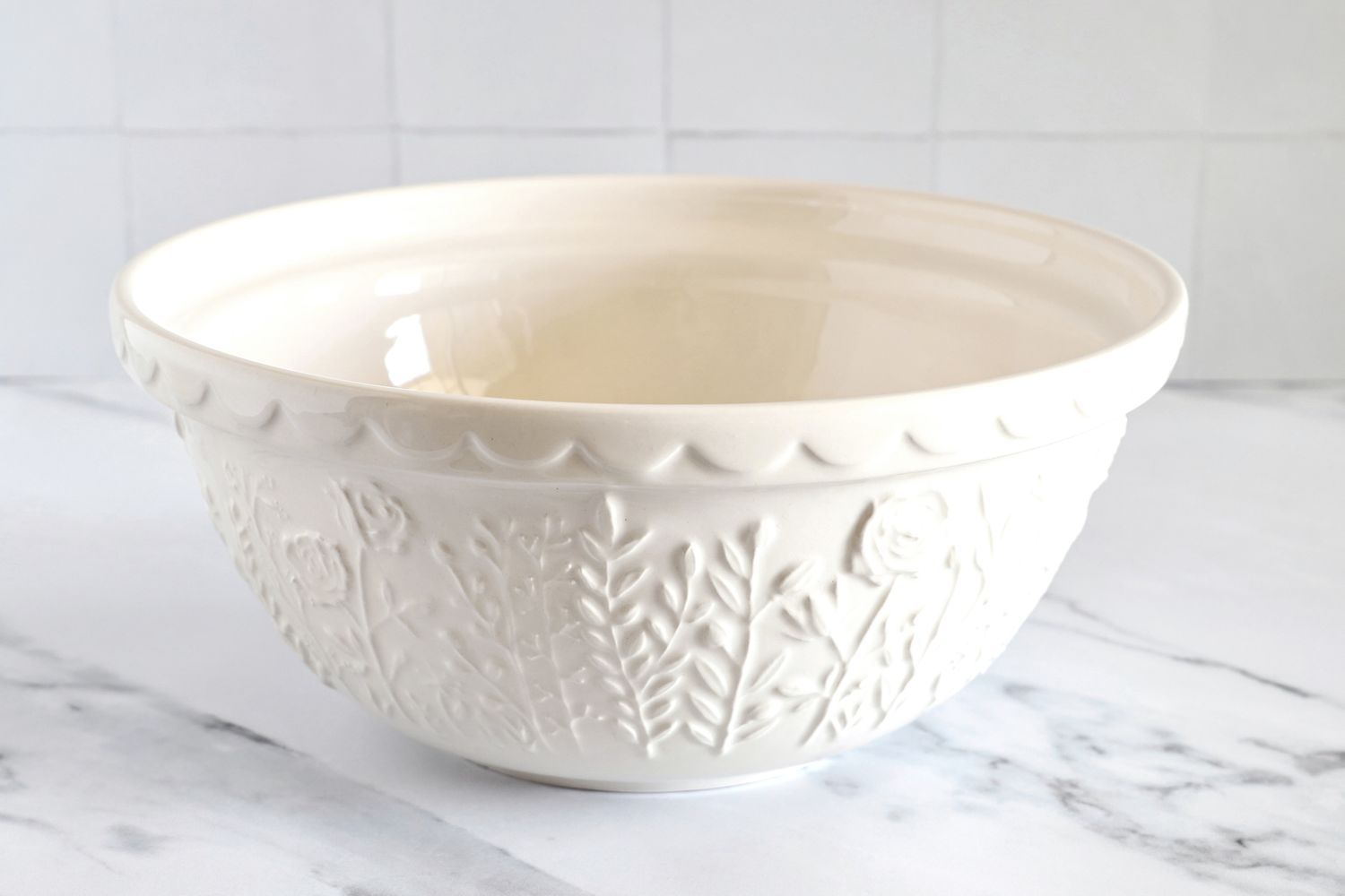 A Mason Cash bowl with embossed floral patterns on the exterior placed on a marble surface