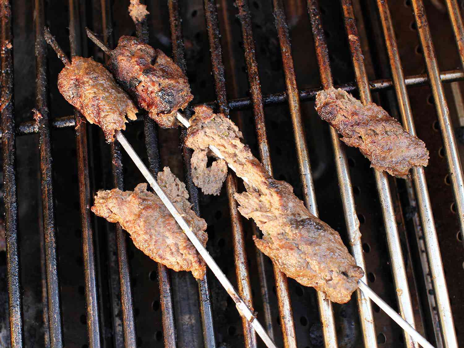 Skewers of seekh kebab on the grilled. The meat has fallen apart. 