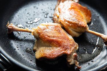 Two duck confit legs in a skillet. 