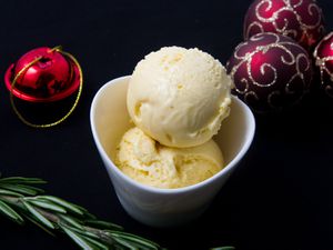 Two scoops of leftover panettone ice cream, served in a small white bowl and surrounded by Christmas tree ornaments and a sprig of basil.