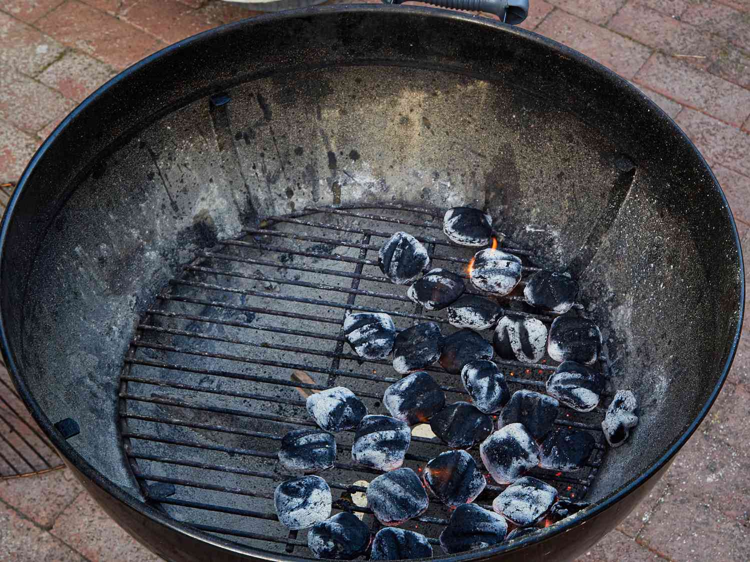 Charcoal grill with partially lit coals arranged on the bottom surface of the grill