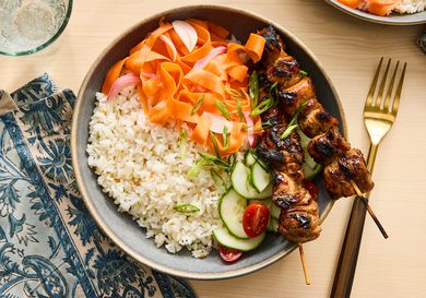 carrot ribbons in a bowl with rice, cucumber and chicken skewers 