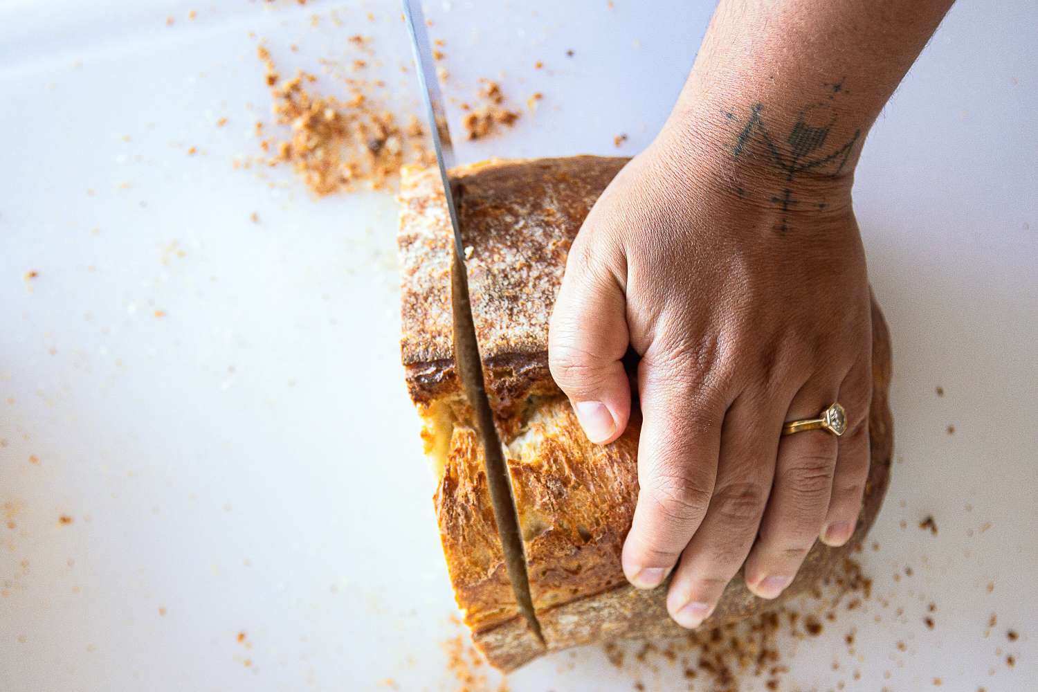 A hand with a ring slicing a loaf of bread on a white surface