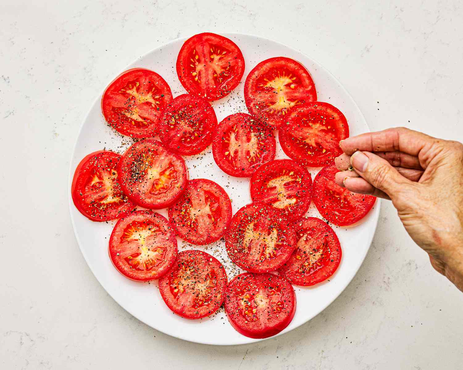 Overhead view of sprinkling tomatoes with pepper