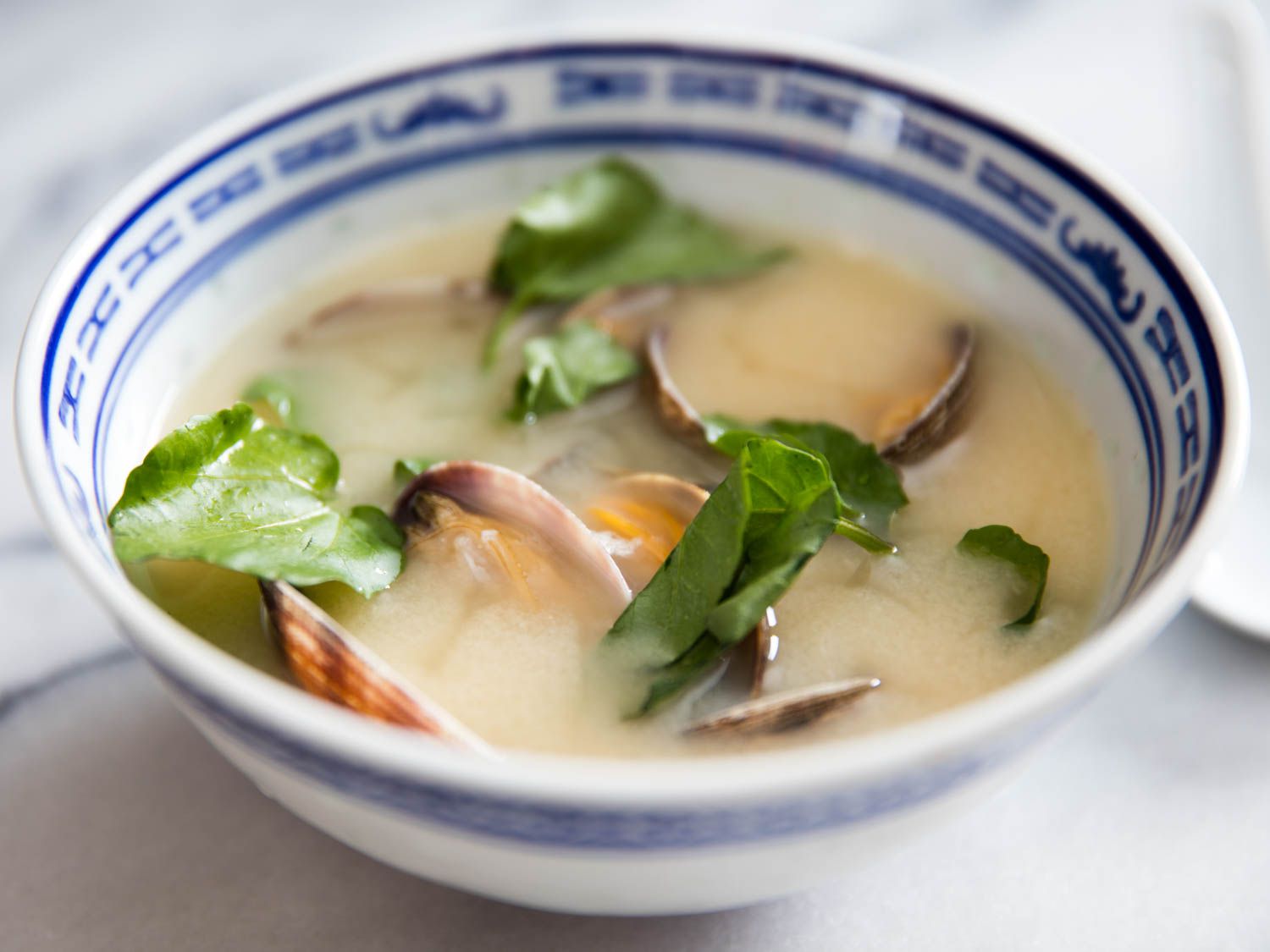 A bowl of miso soup with clams and greens.