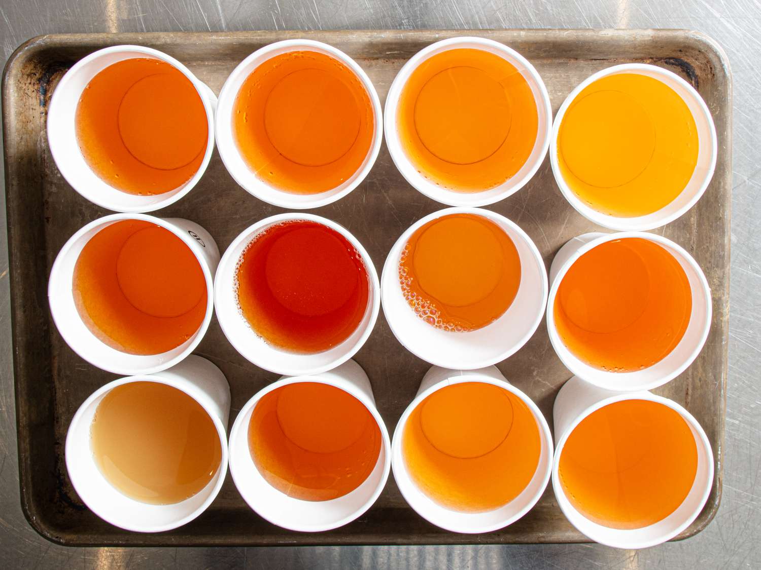 Twelve cups with varying shades of a liquid on a tray