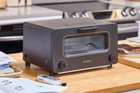 A BALMUDA toaster oven placed on a kitchen counter, surrounded by kitchen items