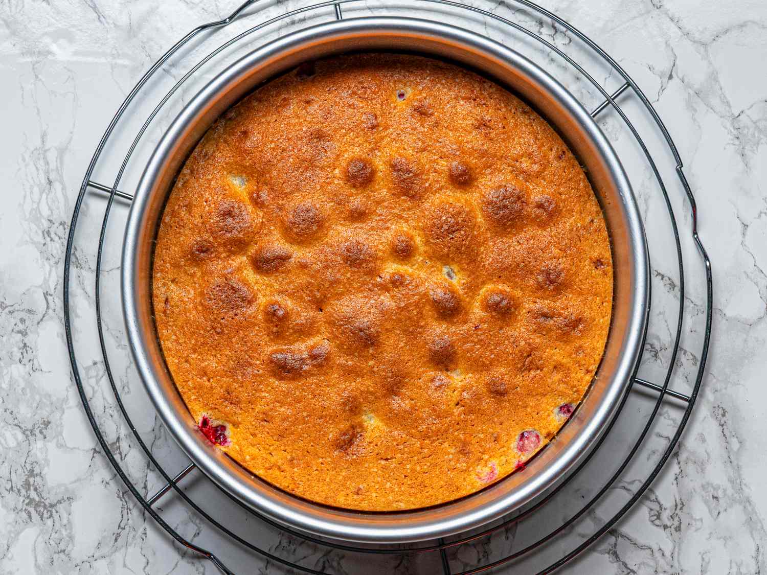 Baked cranberry upsidedown cake in a round pan placed on a cooling rack