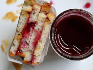 A peanut butter and jelly sandwich next to a jar of grape jam. 