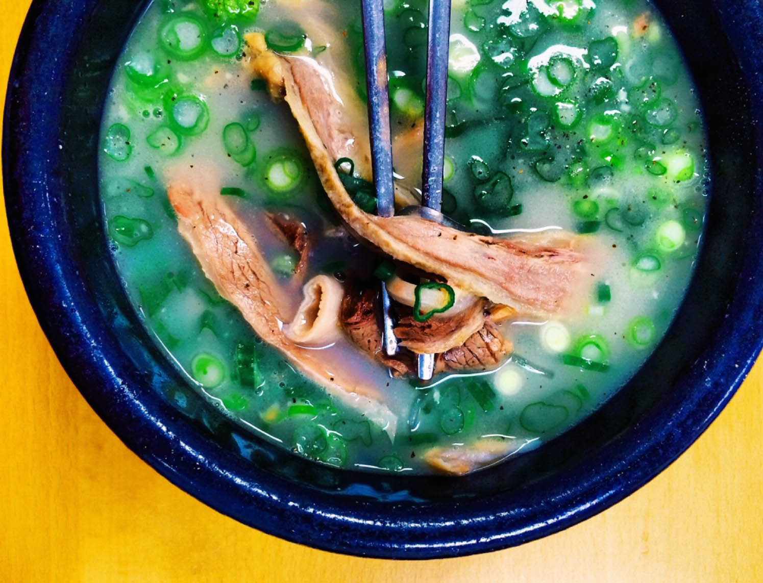 A bowl of seolleongtang, a Korean soup with a milky broth, beef, and translucent glass noodles.