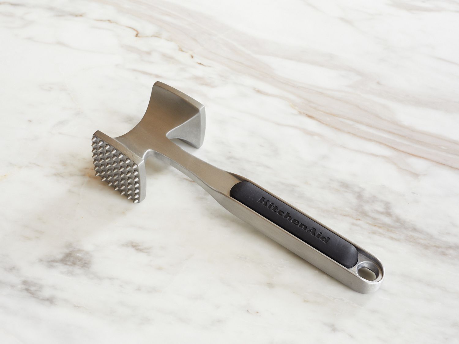 A meat tenderizer tool with a textured side and labeled handle on a marble surface