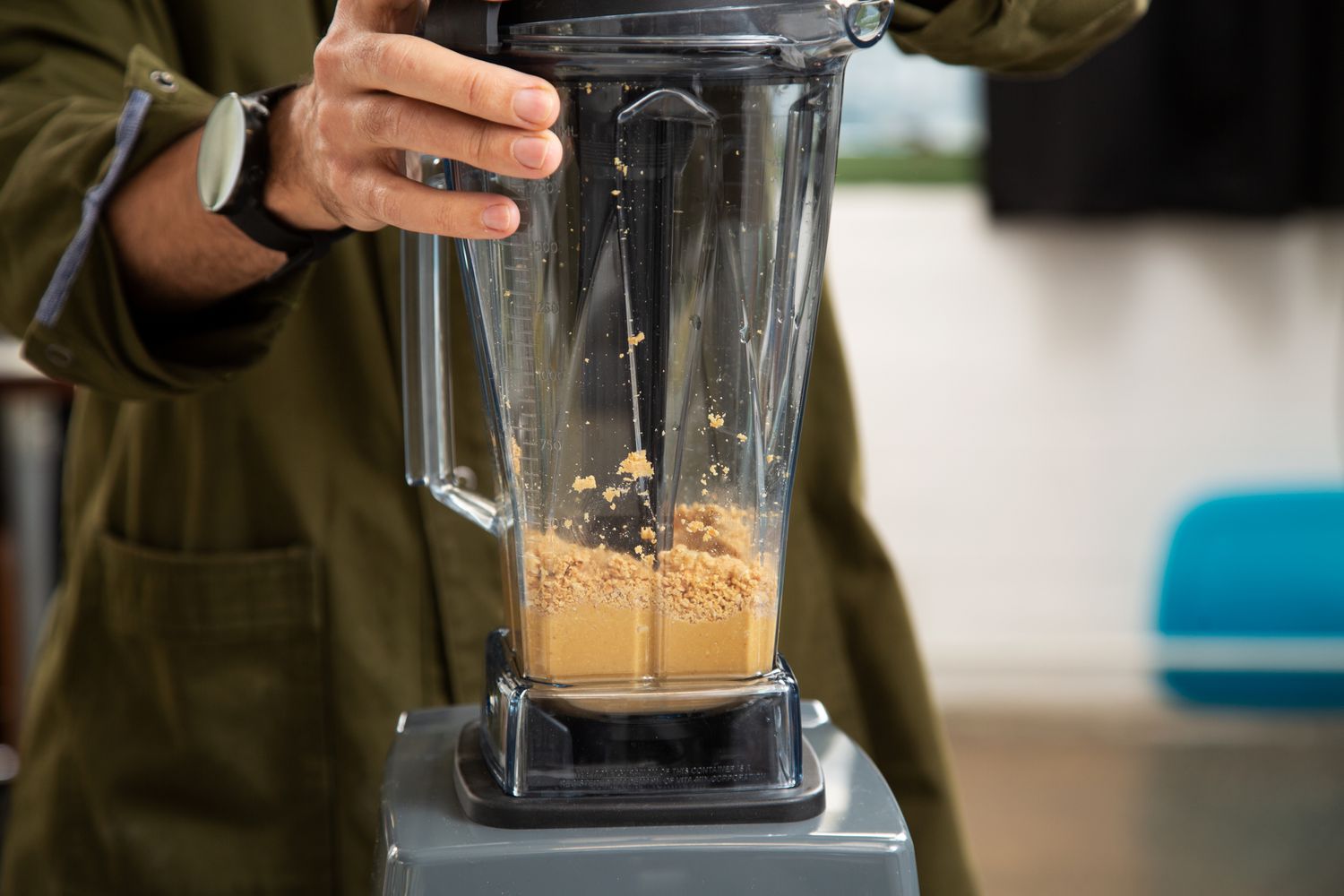 An person using a tamper to make nut butter with a Vitamix blender