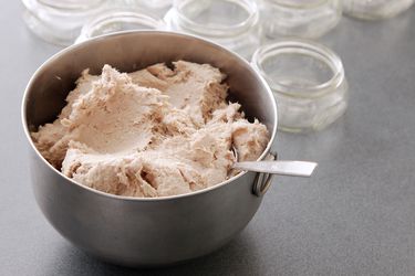 A small metal mixing bowl filled with pork rillettes. Wide-mouth quarter-pint jars are arrayed in the background.