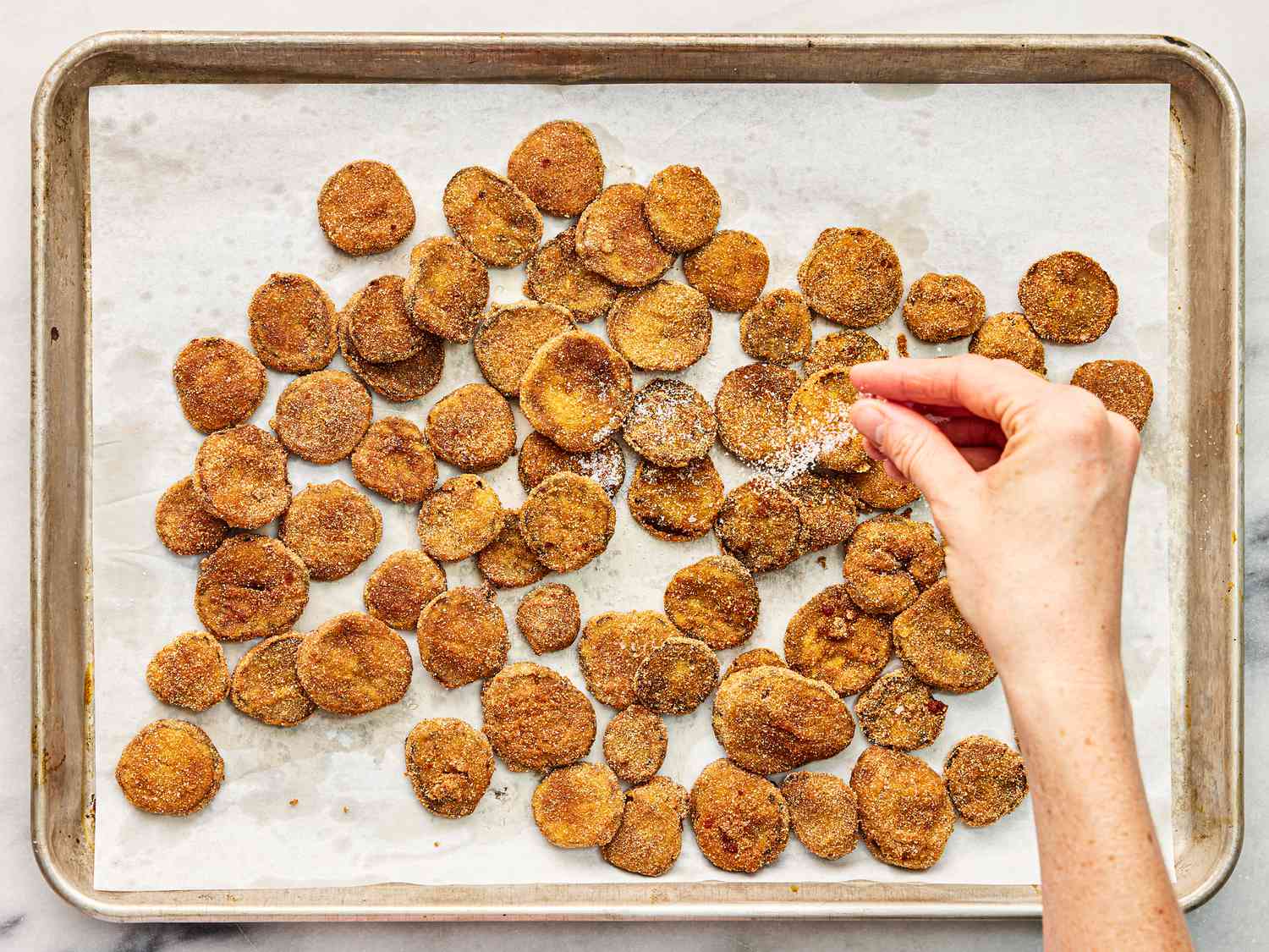 Seasoning fried pickled that are draining on a paper towel lined pan.