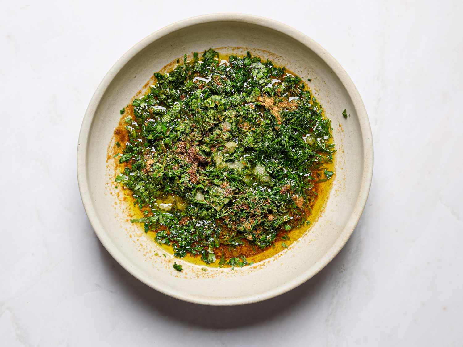 A white bowl containing green herbed chermoula sauce with spices and olive oil