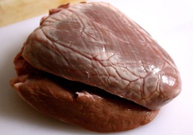 An uncooked beef heart on a white cutting board.