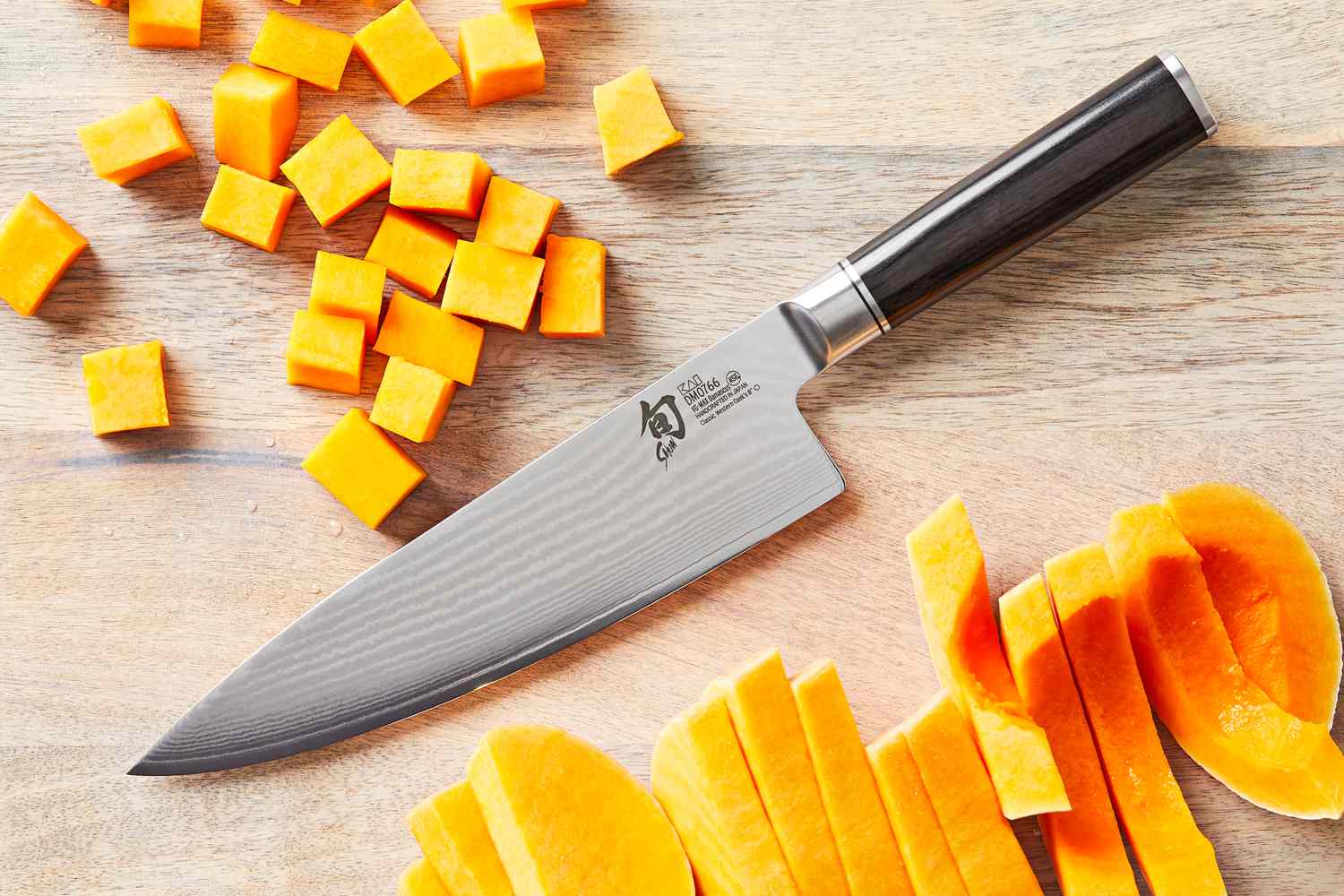 a closeup of the shun chef's knife on a wooden surface with cut up butternut squash