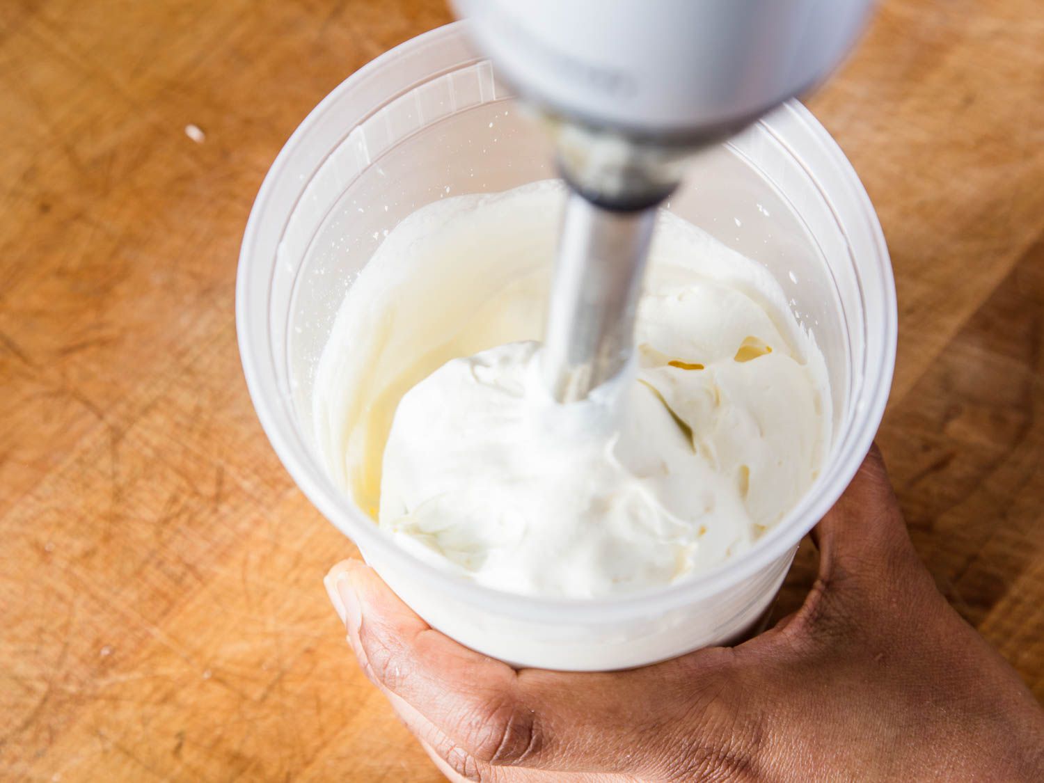 Using an immersion blender to whip cream in a clear plastic container.
