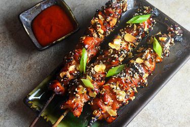 Overhead view of Crispy Caramelized Chicken Skewers, served on a dark green rectangular platter.
