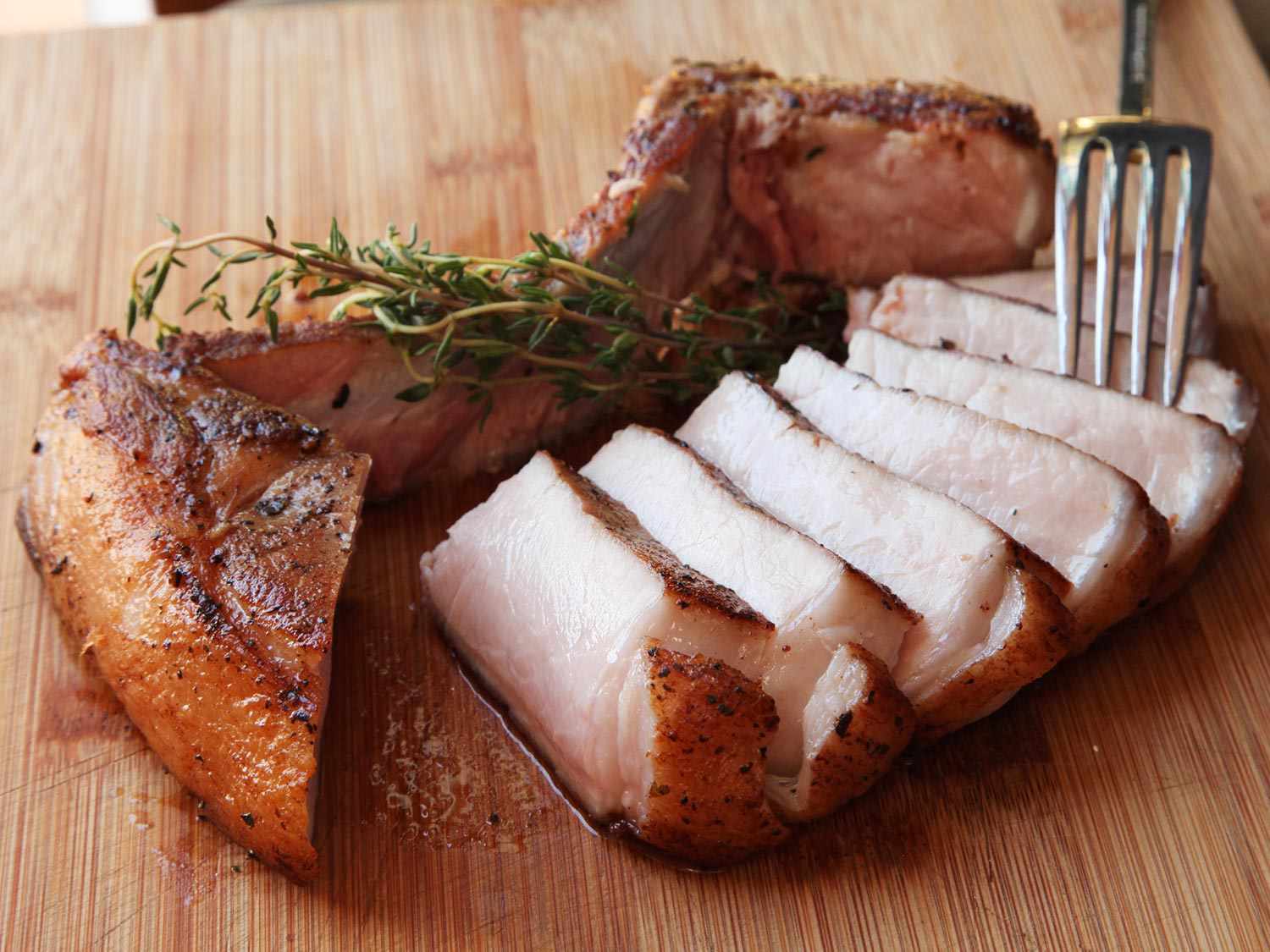 Sliced sous vide pork chops on a cutting board with a sprig of fresh thyme.