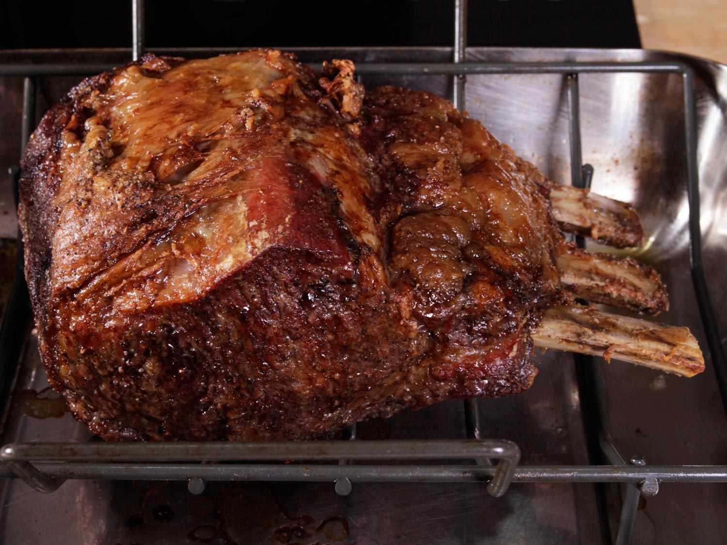 A finished prime rib roast, resting on a rack in a roasting pan.