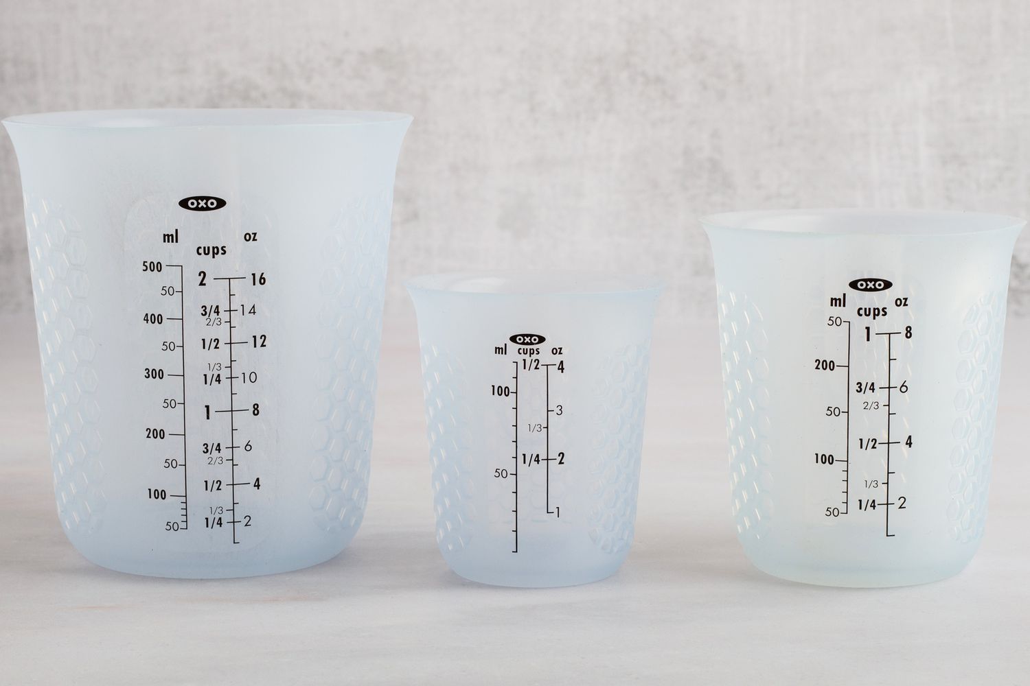 Three silicone OXO liquid measuring cups on a marble kitchen countertop.