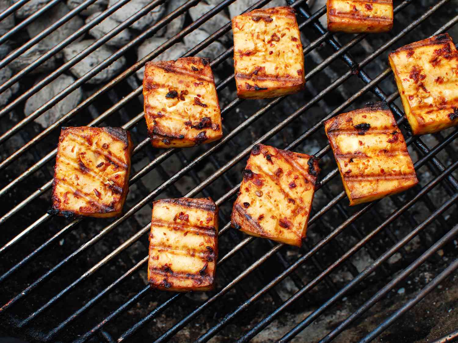 Pieces of marinated tofu on a charcoal grill with char marks.