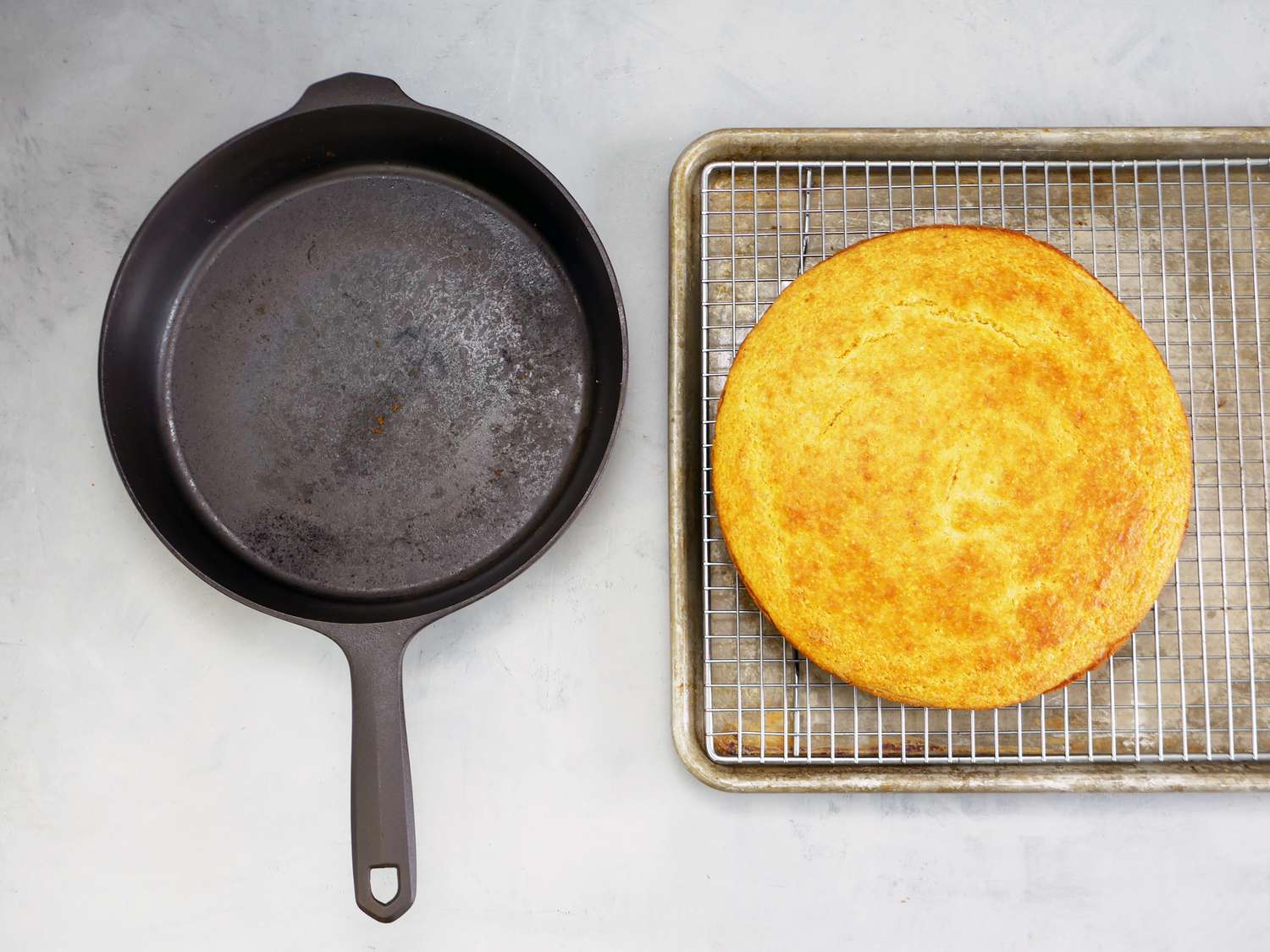 the field co skillet on a gray surface with cornbread on a wire rack in a sheet pan next to it. 