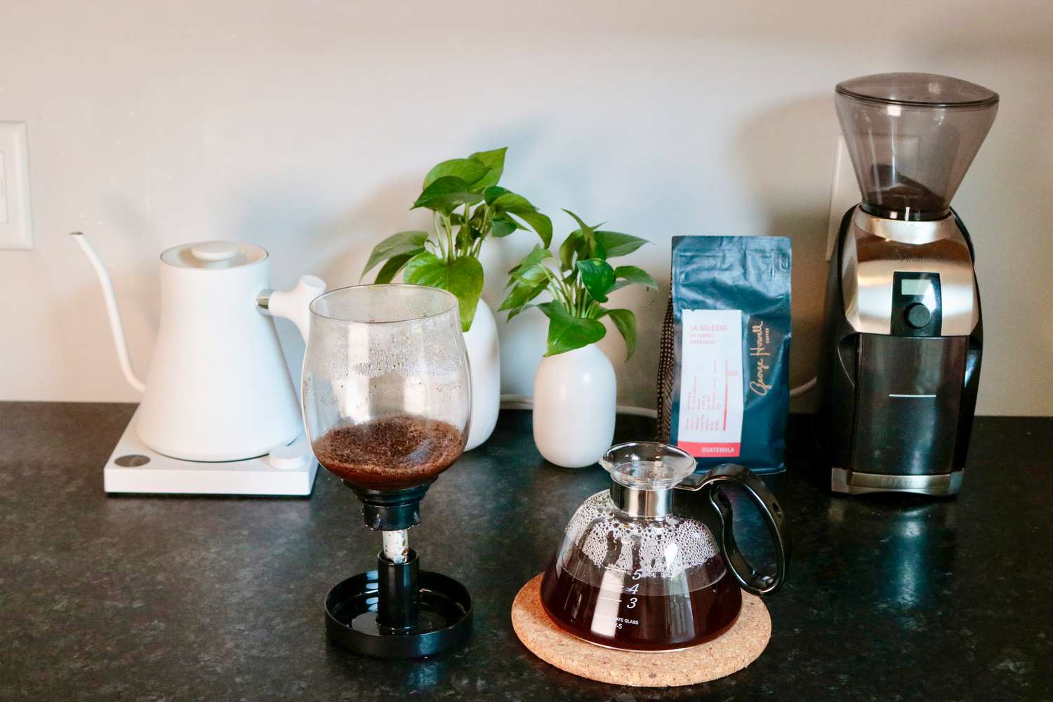 A siphon burner with its base on a cork trivet and its top set to the side