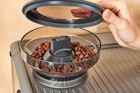 A person lifting up the coffee grinder lid of the Breville Barista Express Impress