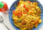 A bowl of curried Singapore rice noodles with char siu, shrimp, bell peppers, and vegetables. 