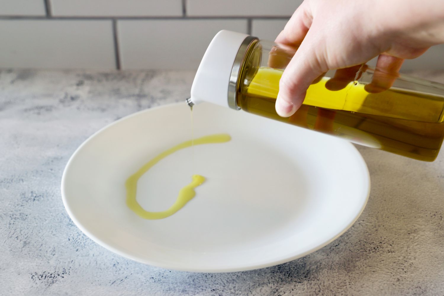 A person pouring oil from the OXO Precision Pour Glass Dispenser