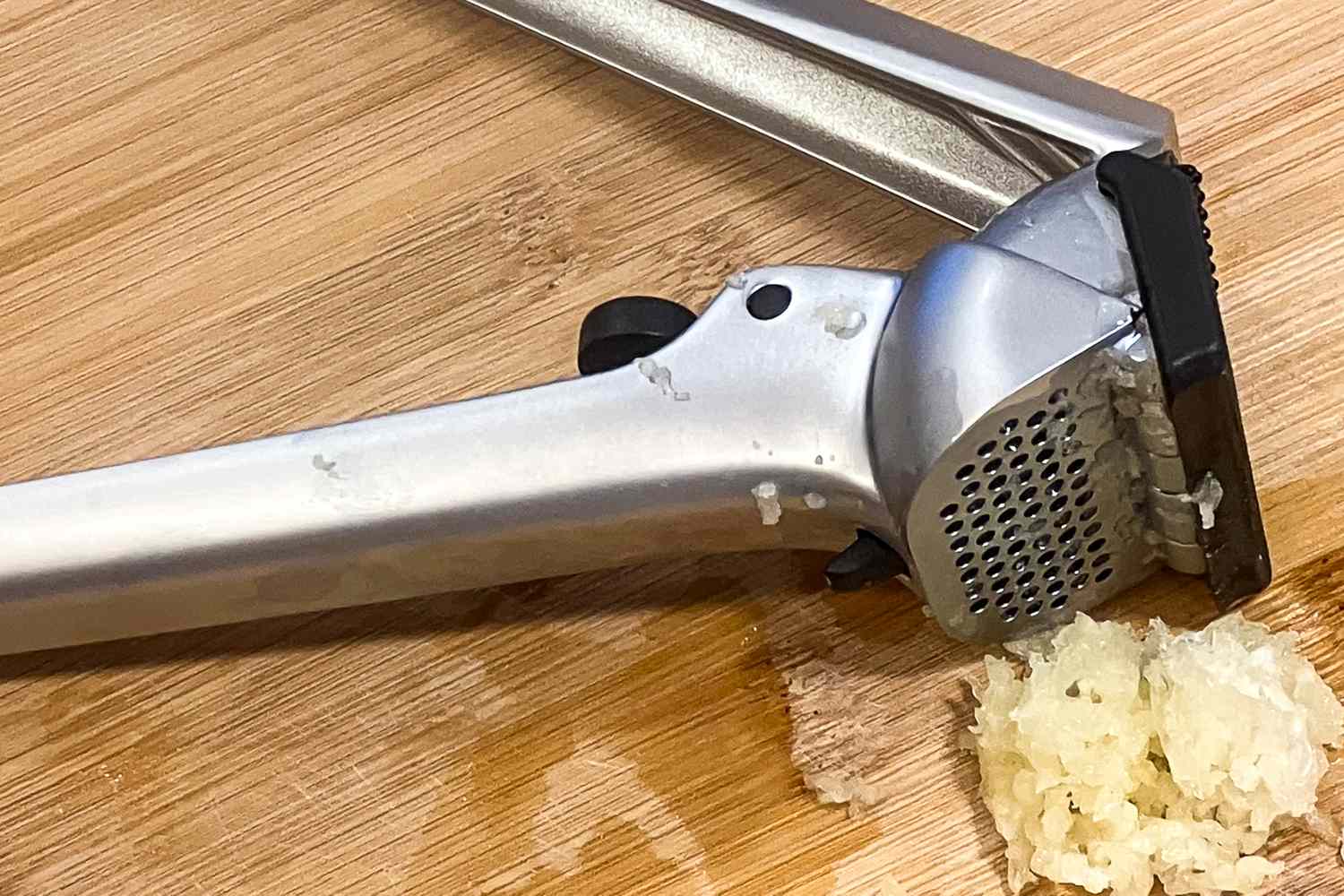 A garlic press on a wooden surface with pressed garlic beside it
