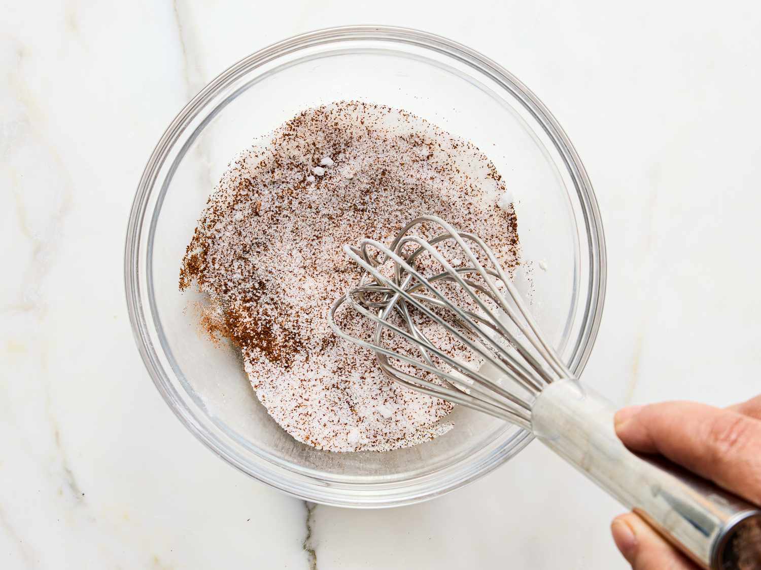 A clear bowl with dry ingredients being whisked together by hand for gingerbread latte cookies