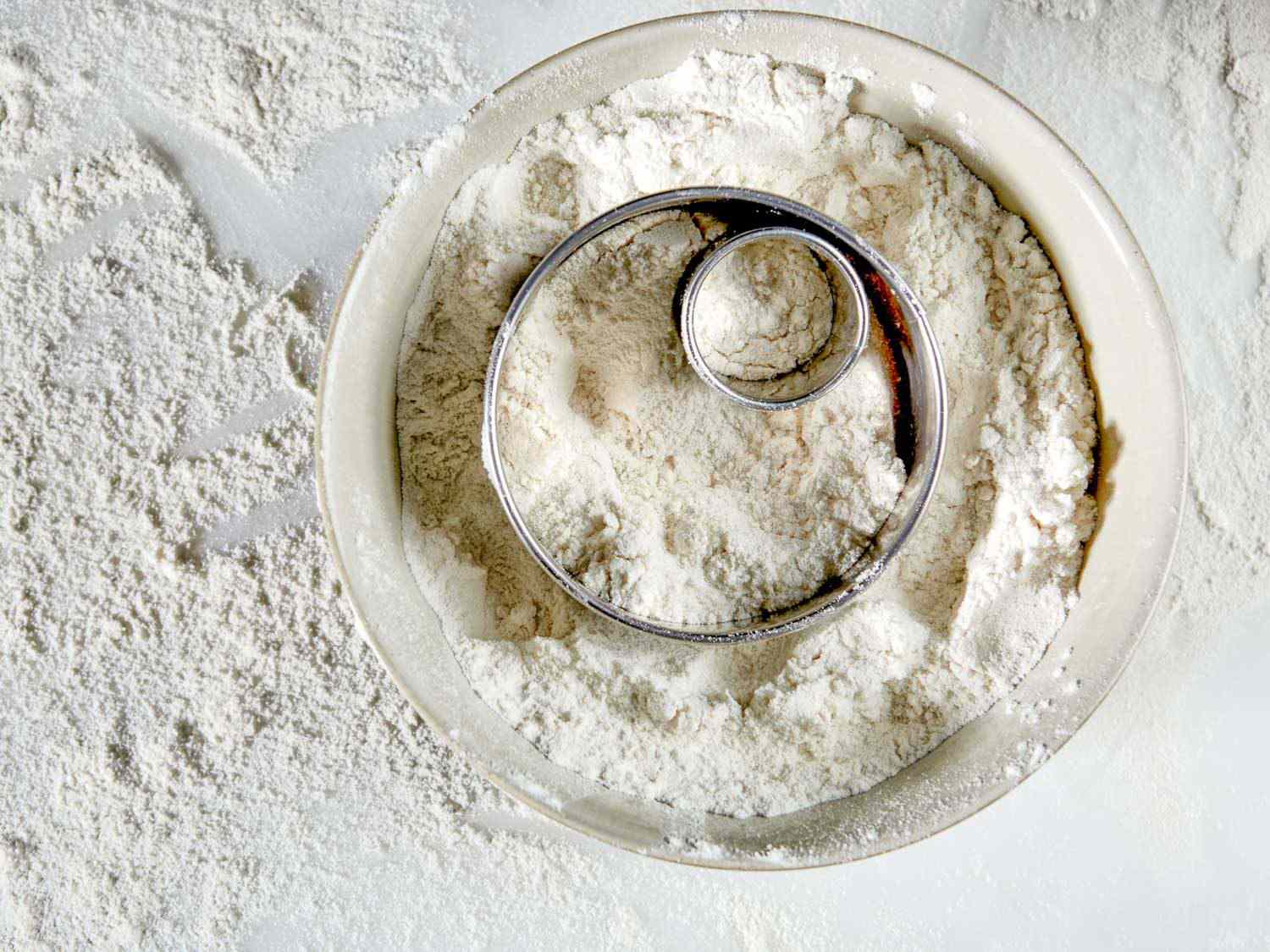 cookie cutters for making doughnuts, resting in a bowl of flour