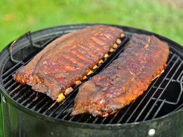 Two racks of barbecued pork spareribs sitting on the grate of a smoker.