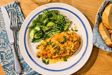 A plate with chicken paillard and a side of greens, placed on a wooden table with a fork and a napkin