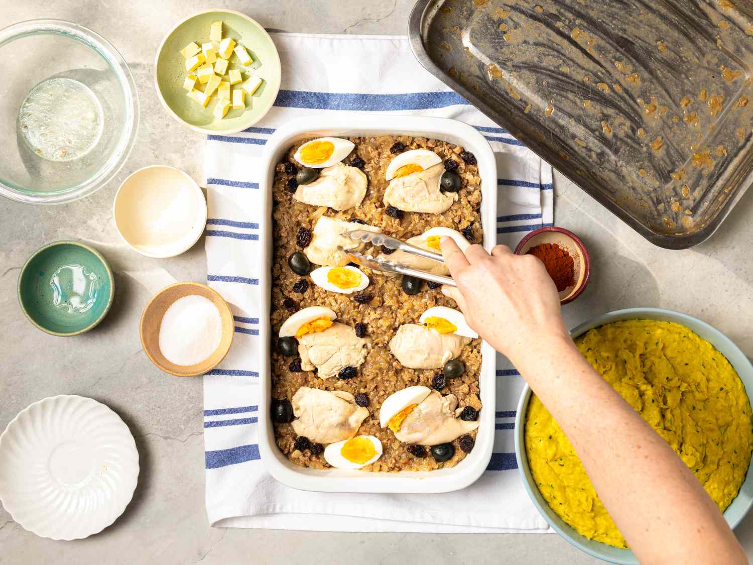 Arranging chicken, egg, olives and raisins on top of beef later in baking dish