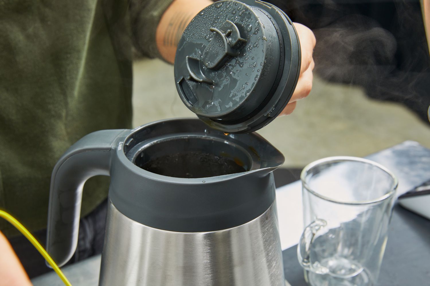 The lid being removed from a stainless steel coffee carafe.