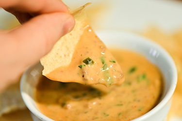 A tortilla chip is dunked in a small bowl of taco queso dip.