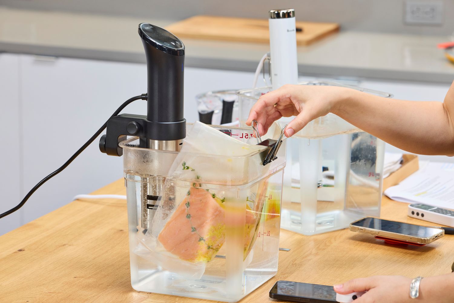 Anova Culinary Precision Cooker 3.0 cooking food in a vacuum-sealed bag immersed in water, with a person adjusting a clip on the bag