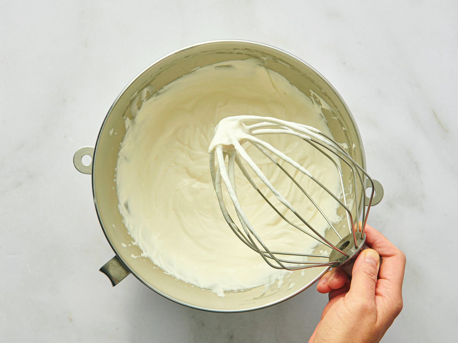 Cream mixture in a bowl with hand holding a whisk