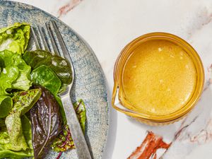 Lemon vinaigrette in a small bowl next to a plate of greens.