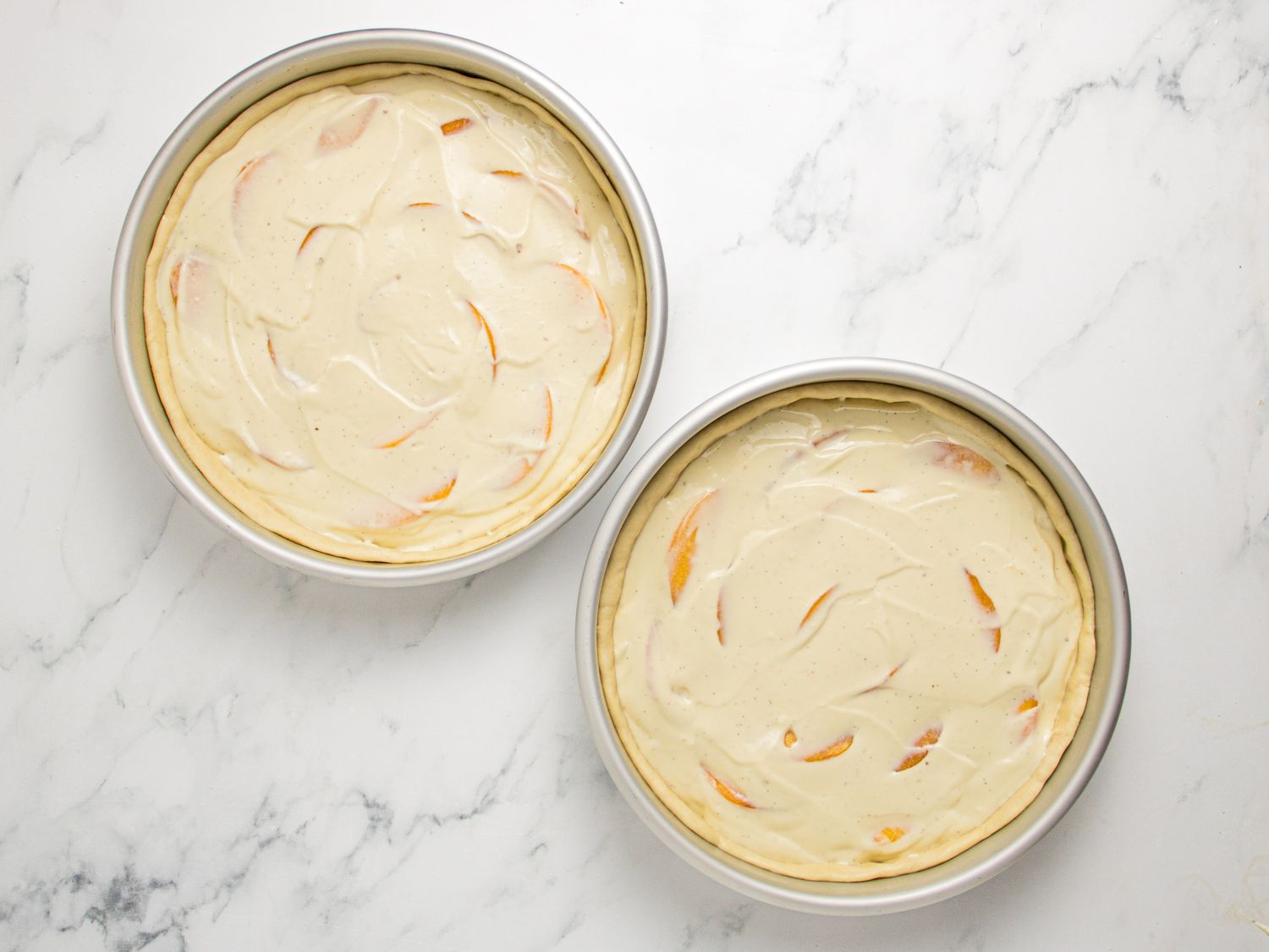 Two round cake batterfilled pans on a marble countertop