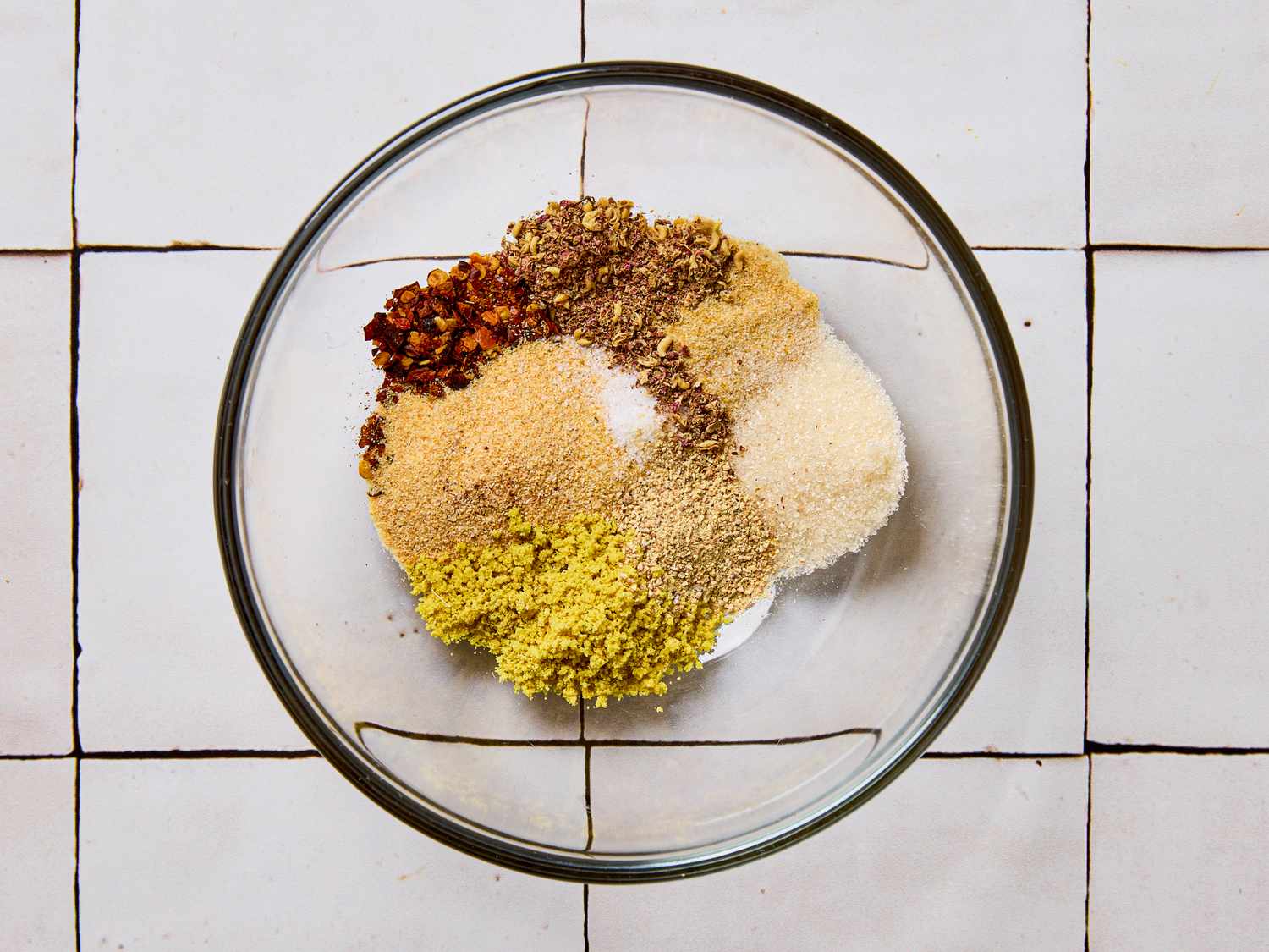 A clear glass bowl containing various ground spices arranged separately