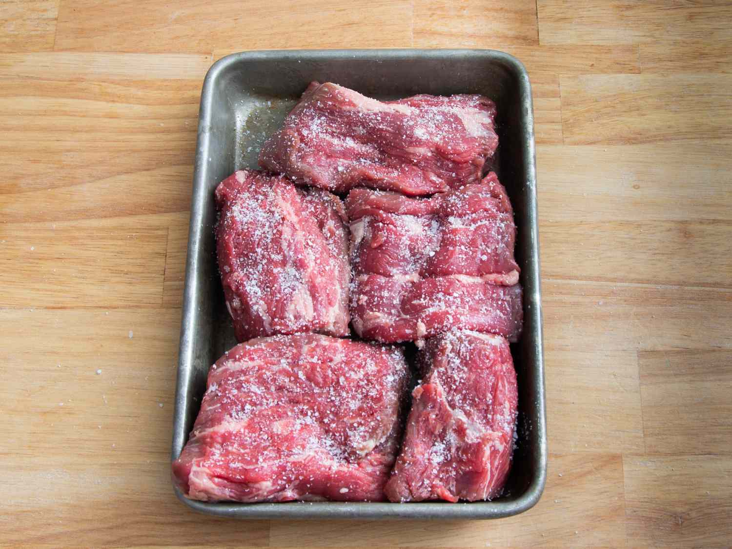 Salted raw pieces of beef in a baking pan. 